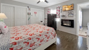 A bedroom with a bed, a ceiling fan, a refrigerator, a fireplace, and a door with a 'No Smoking' sign.