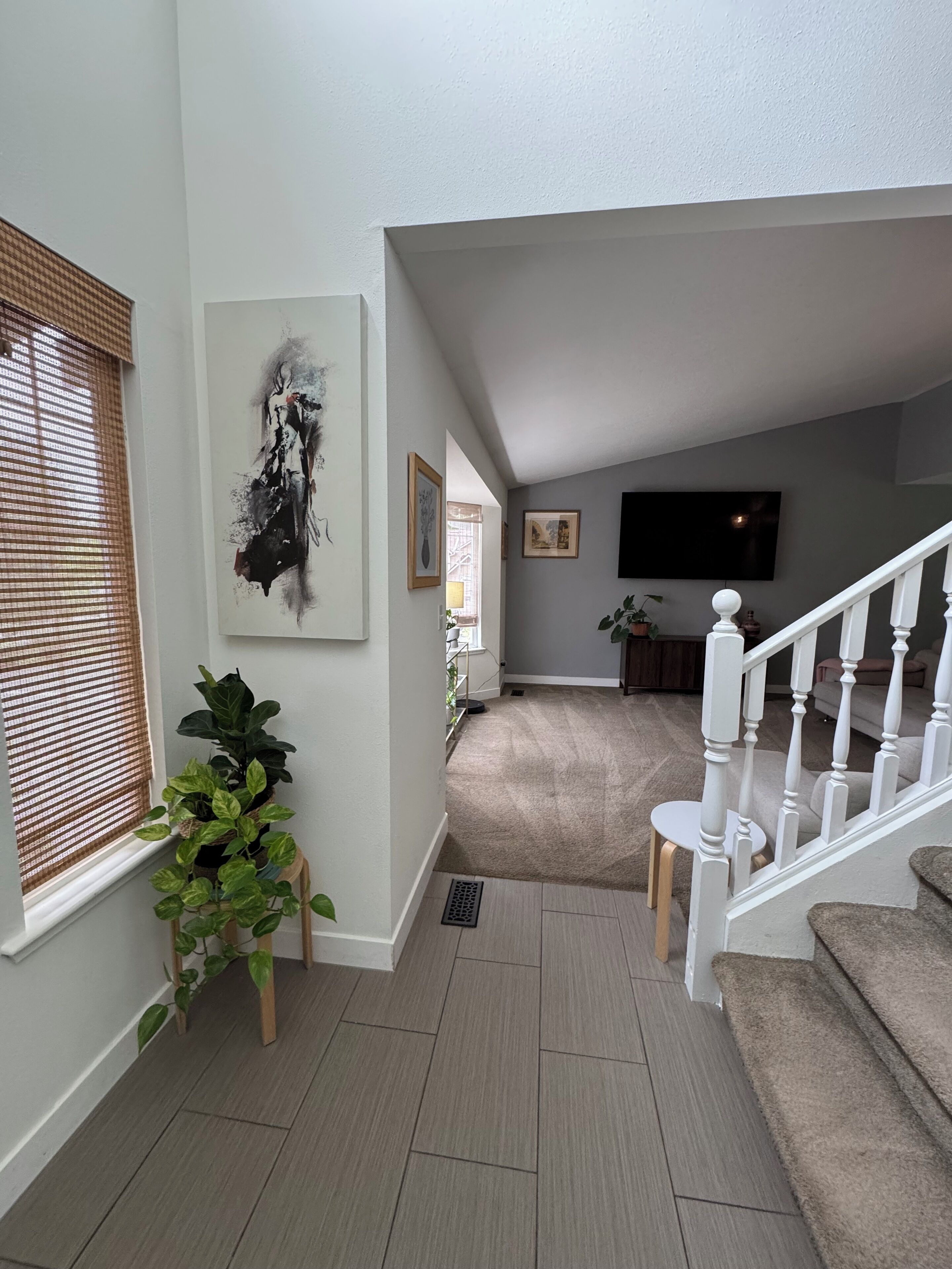 A modern living room with a staircase, a large painting, and a potted plant.