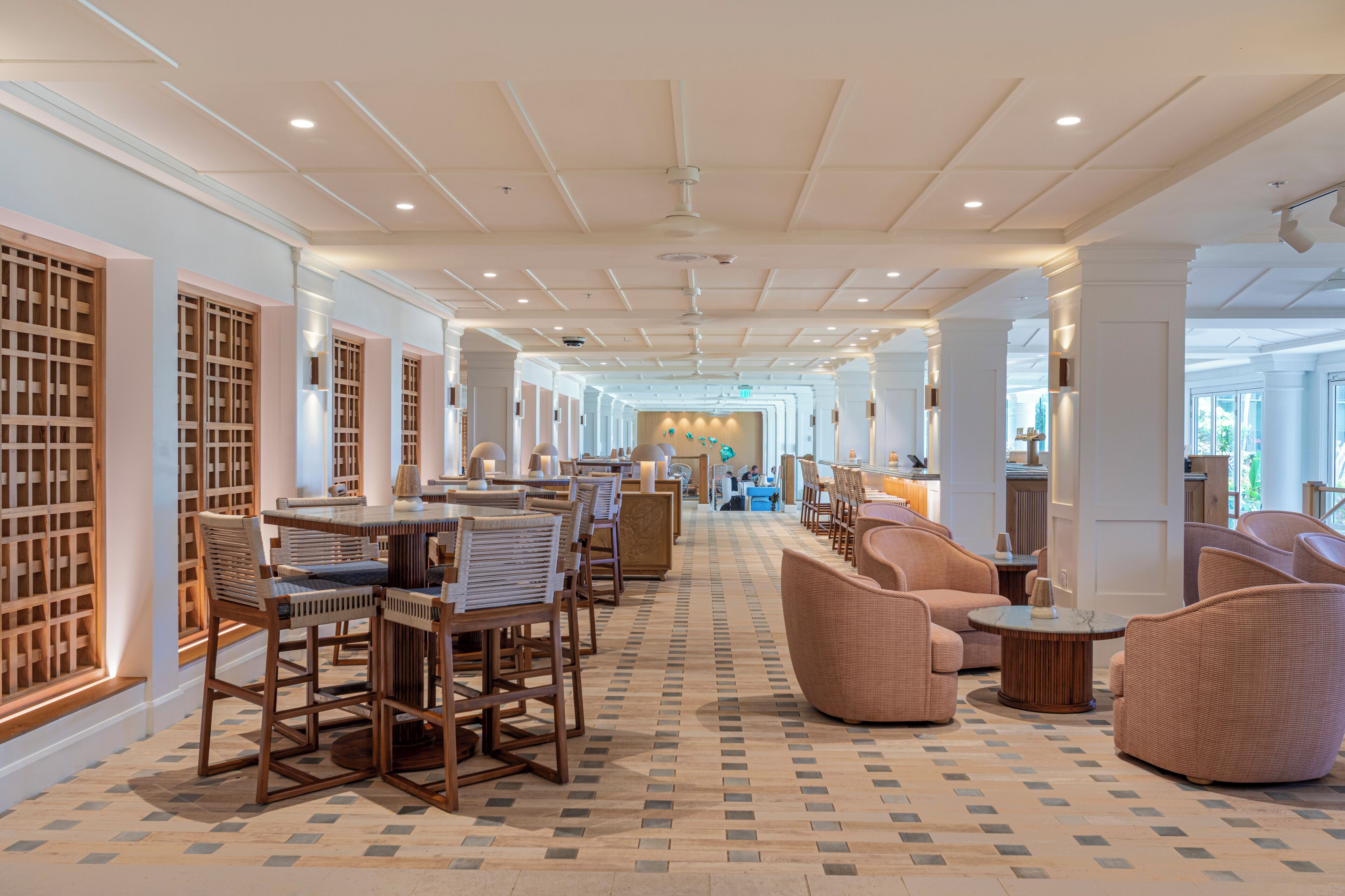 A hotel lobby with a long corridor, wooden furniture, and a patterned floor.