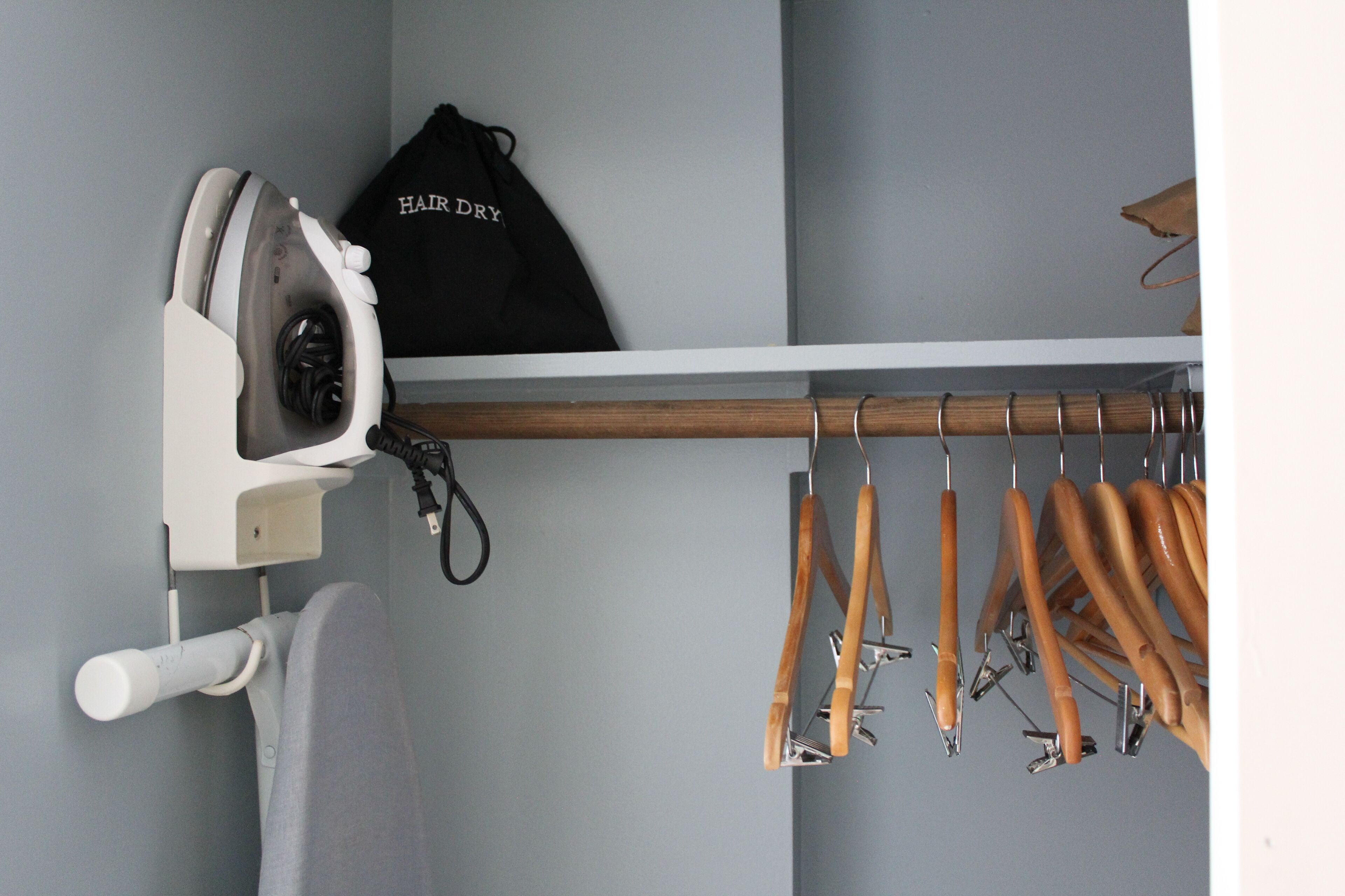 Un armario con una percha para ropa, una tabla de planchar blanca y un bolso negro con la etiqueta "HAIR DRY".
