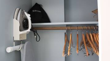 Un armario con una percha para ropa, una tabla de planchar blanca y un bolso negro con la etiqueta "HAIR DRY".