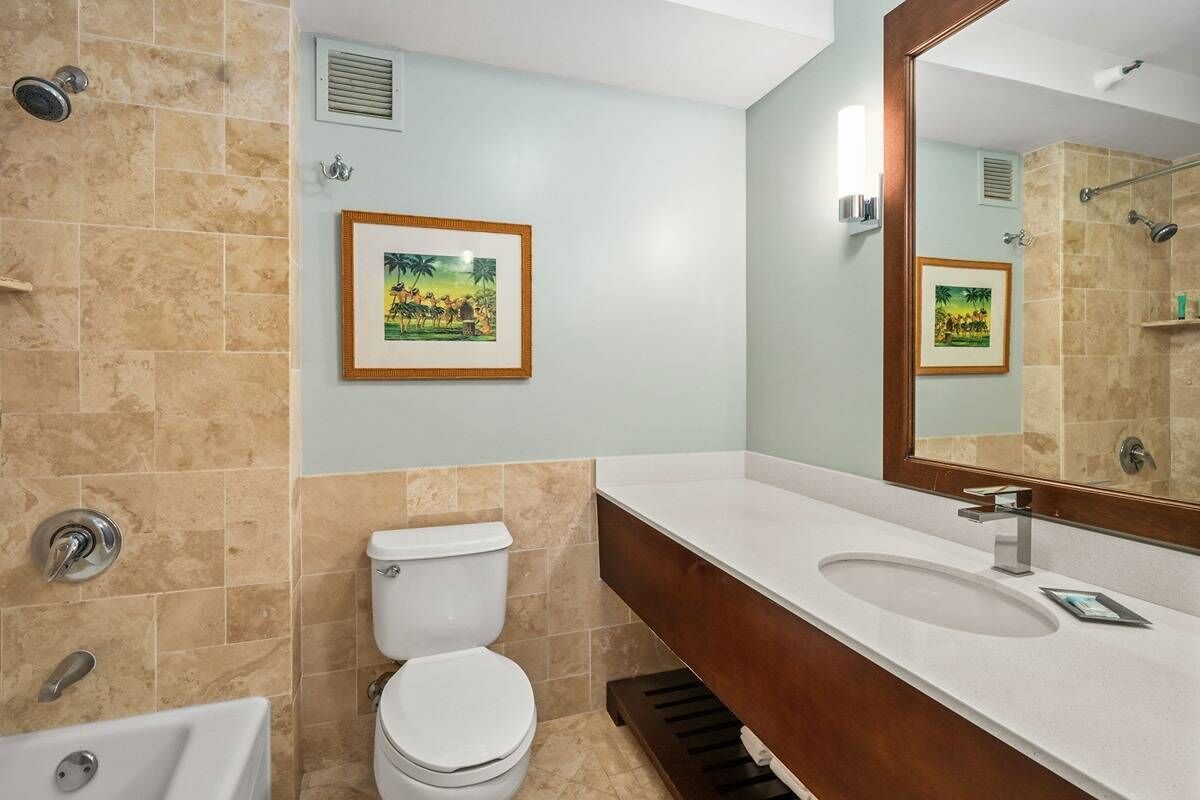 Ein Badezimmer mit Toilette, Waschbecken und Dusche. An den Wänden befinden sich Bilder in Rahmen.