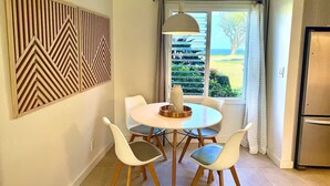 A dining area with a round table, four chairs, a decorative wall panel, and a view of the outdoors through a window with curtains.