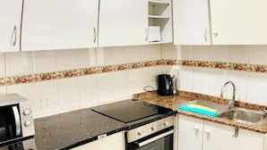 Una cocina con armarios blancos, encimera negra, estufa y fregadero.