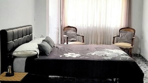 Un dormitorio con cama, dos sillas, una mesita de noche y una ventana con cortinas.