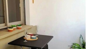 Un pequeño balcón con una mesa para dos, una ventana y una planta en maceta.