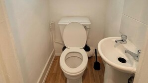 Pieni, siisti kylpyhuone, jossa on wc, pesuallas ja ikkuna wc:n yläpuolella.