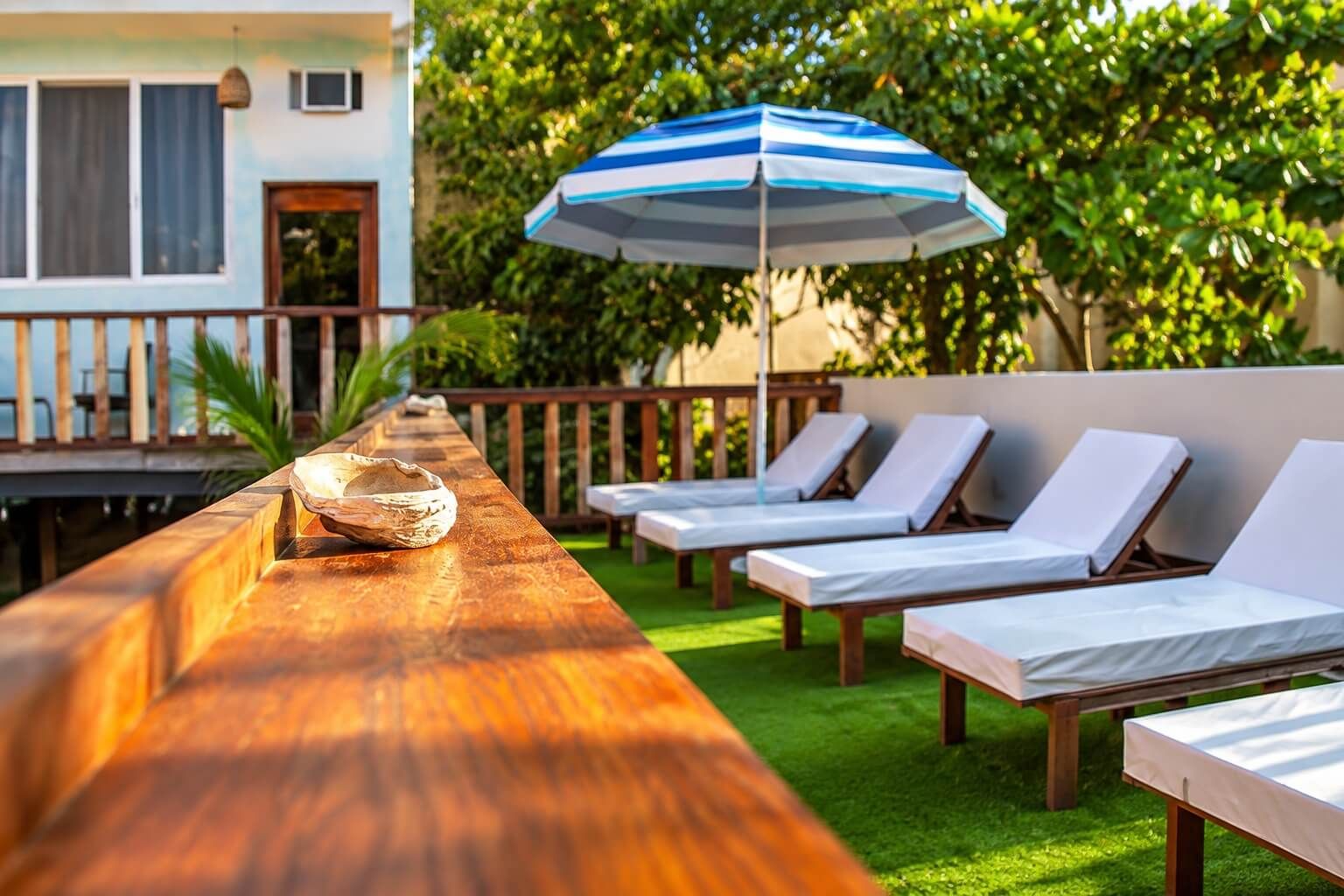 Un espace extérieur ensoleillé, aménagé avec une table en bois, des fauteuils confortables et un parasol à rayures.