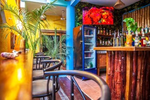 Een bar met zitplaatsen, een koelkast vol flessen en een televisiescherm dat kleurrijk beeldmateriaal toont.
