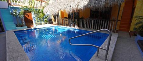 Una piscina con escalera metálica, rodeada por una valla de madera y una estructura de techo de paja.