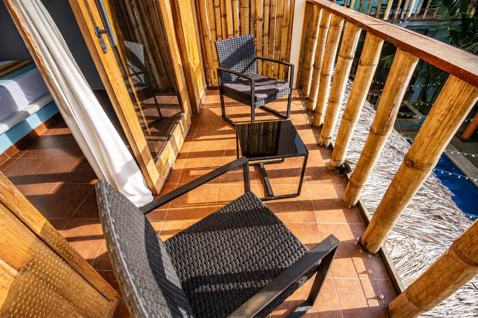 Un balcón con barandilla de madera, una silla de mimbre negro, una mesa a juego y vistas a una piscina.