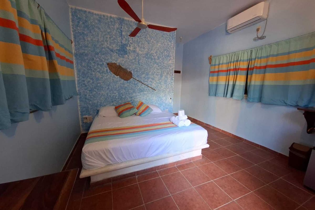 Een hotelkamer met een bed, gestreepte gordijnen, een plafondventilator en een airconditioningsysteem.
