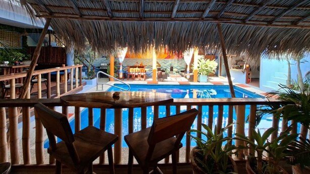 Un espace aménagé au bord de la piscine, doté d’un toit de chaume, de chaises en bois et offrant une vue sur la piscine.