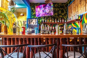 Un bar con mostrador de madera, taburetes y una pantalla de televisión.