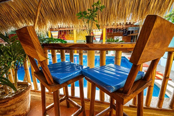 A wooden deck with two chairs and a table, overlooking a pool area. - Zipoliteville (San Pedro Pochutla)