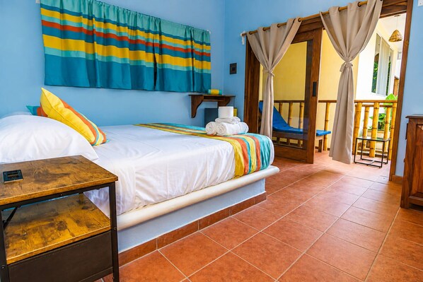 A hotel room with a bed, a wooden nightstand, a colorful striped curtain, and a view of the outside.