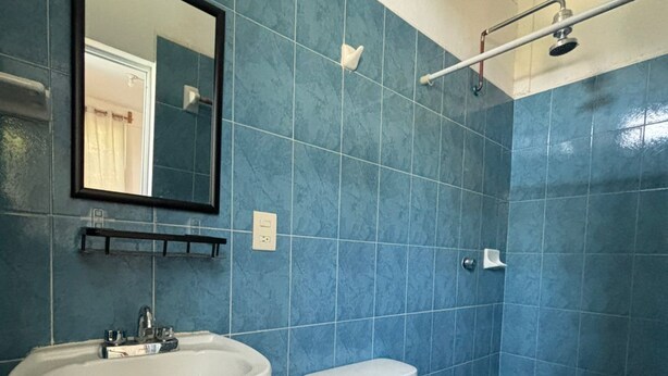 Une salle de bain avec des carreaux bleus, un lavabo blanc, des toilettes et un espace douche.