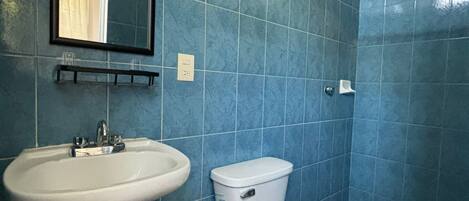 Un baño con azulejos azules, un lavamanos blanco, un inodoro y una zona de ducha.