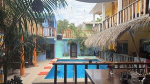 Un espace piscine doté d’une terrasse en bois, de sièges et d’une structure couverte d’un toit de chaume.