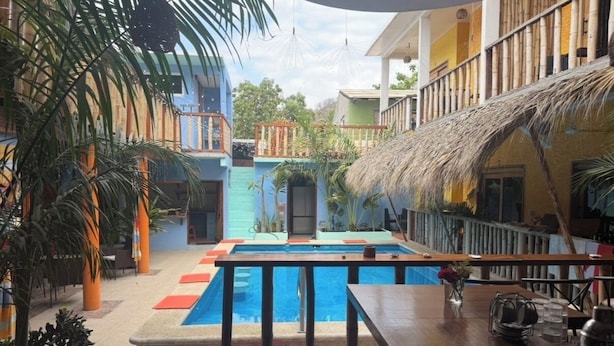 A pool area with a wooden deck, seating, and a thatched roof structure. - Zipoliteville (San Pedro Pochutla)