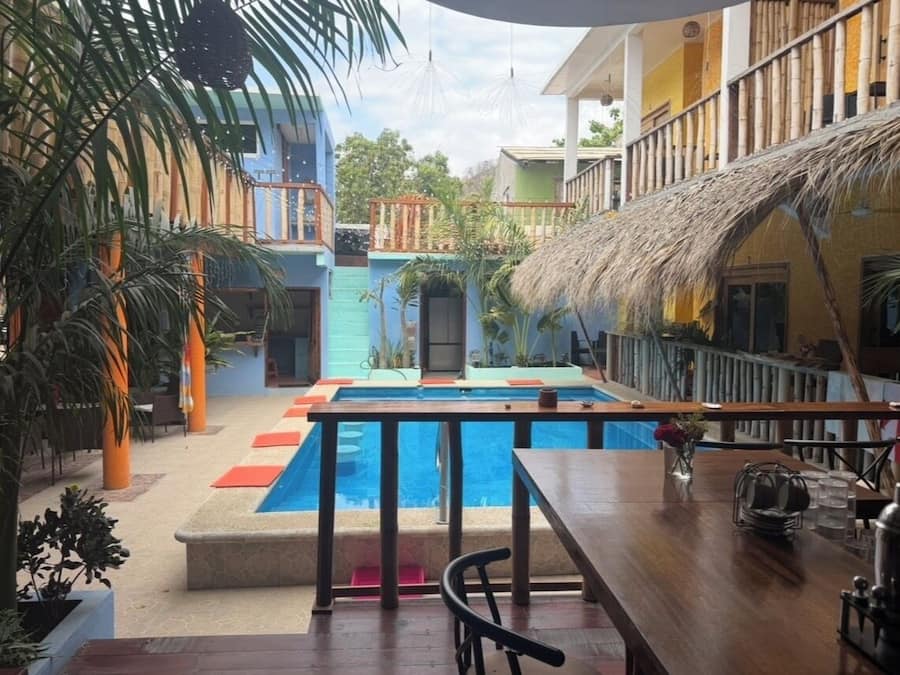 Uma área de piscina com deck de madeira, assentos e estrutura de telhado de palha.
