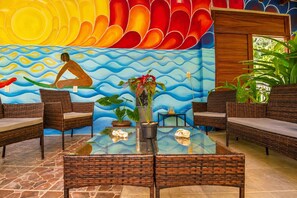 Una habitación con muebles de mimbre, una mesa de vidrio y un mural con una persona practicando surf.