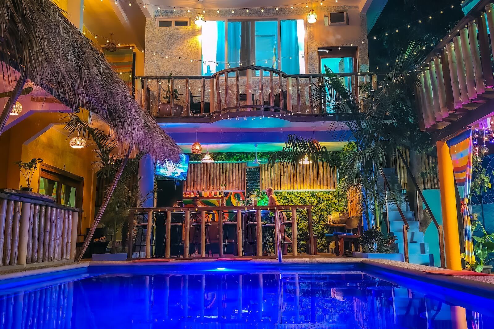 Área interna de piscina com bar e assentos, decorada com bambu e plantas.