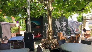 Un espace extérieur aménagé en terrasse, avec des tables et des chaises, un arbre décoratif et une fresque murale.
