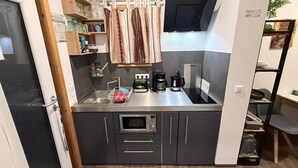 Une cuisine compacte équipée d’un four à micro-ondes encastré, d’une machine à café et d’un grille-pain. On y trouve un petit évier et un meuble contenant de la vaisselle.