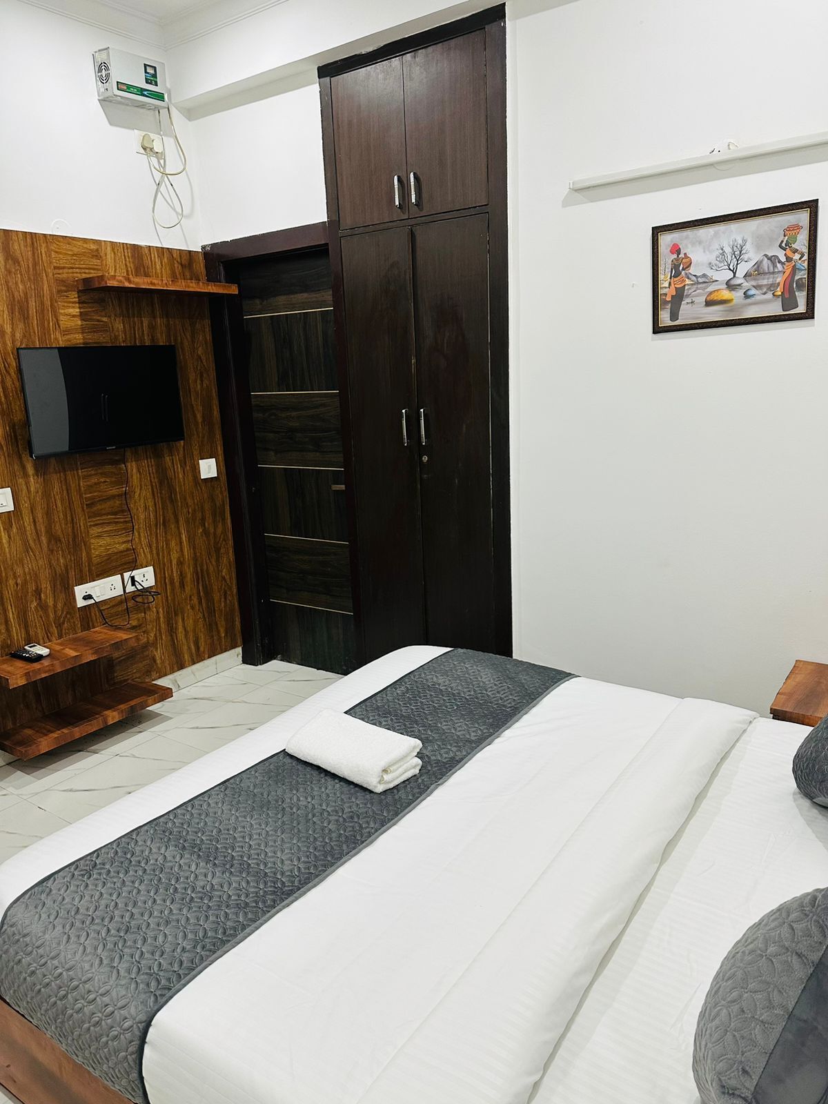 Ein Schlafzimmer mit einem Bett, einem an einer Holzplatte montierten Fernseher, einem Kleiderschrank und einem Bild an der Wand.
