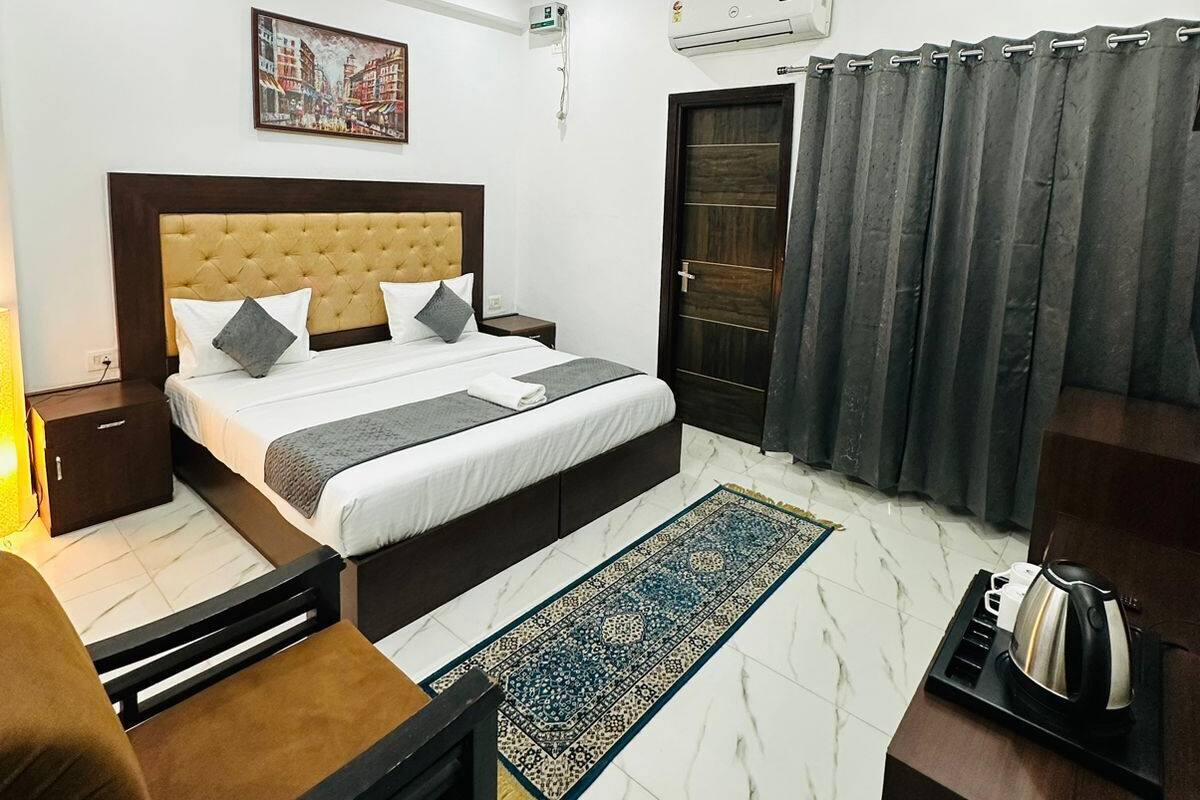 A modern bedroom with a tufted headboard bed, a ceiling fan, an air conditioning unit, a dark wooden door, and a patterned rug.