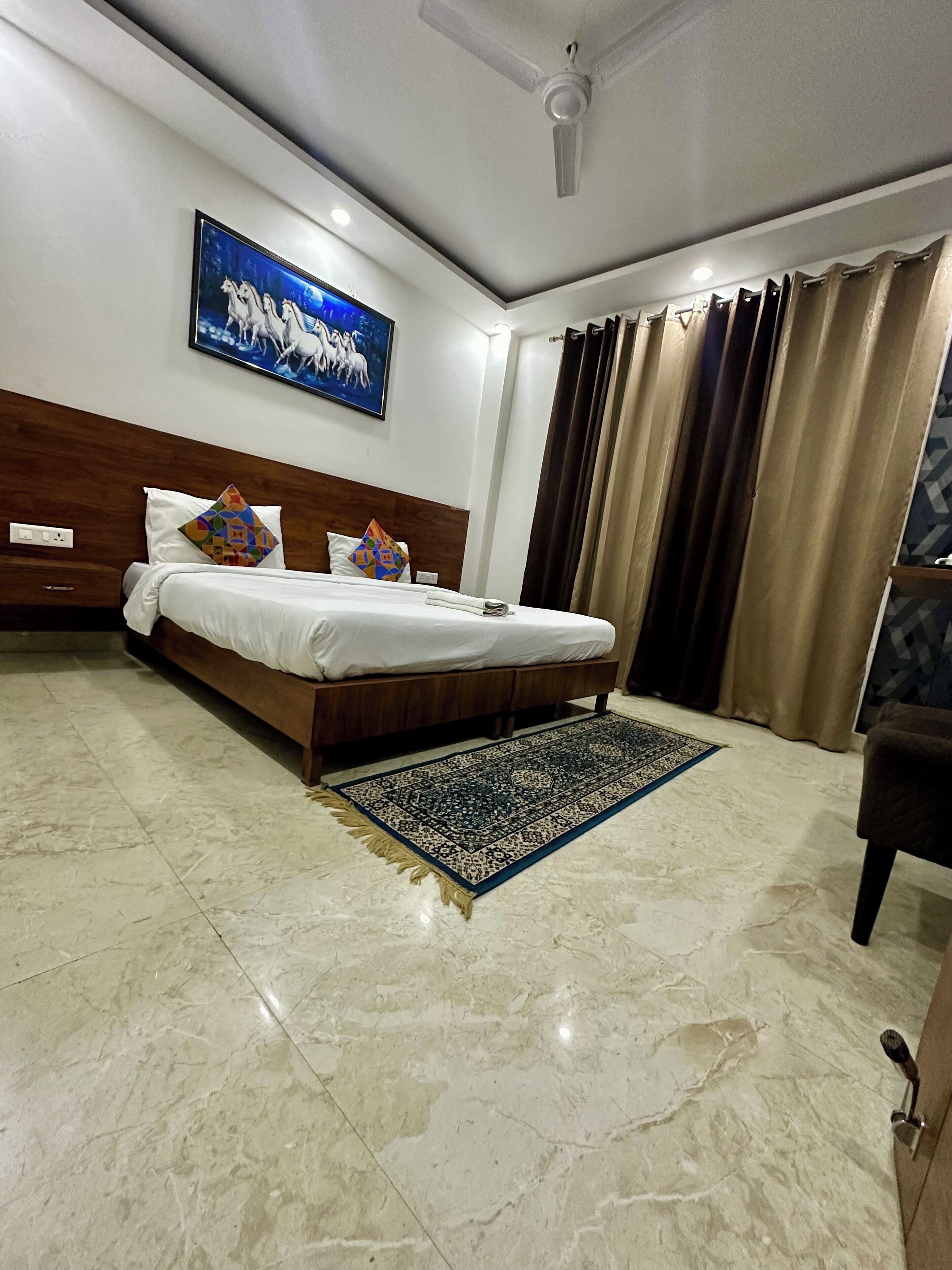 Una camera d'albergo con un letto, una ventola a soffitto, un quadro, un tappeto e delle tende.