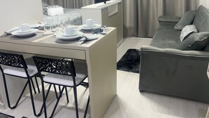 A modern living room with a dining area, grey sofa, flat-screen TV, and a table set for two. - Studio 5 minutes from the Metro, Expo Center Norte, Anhembi (Tucuruvi São Paulo)