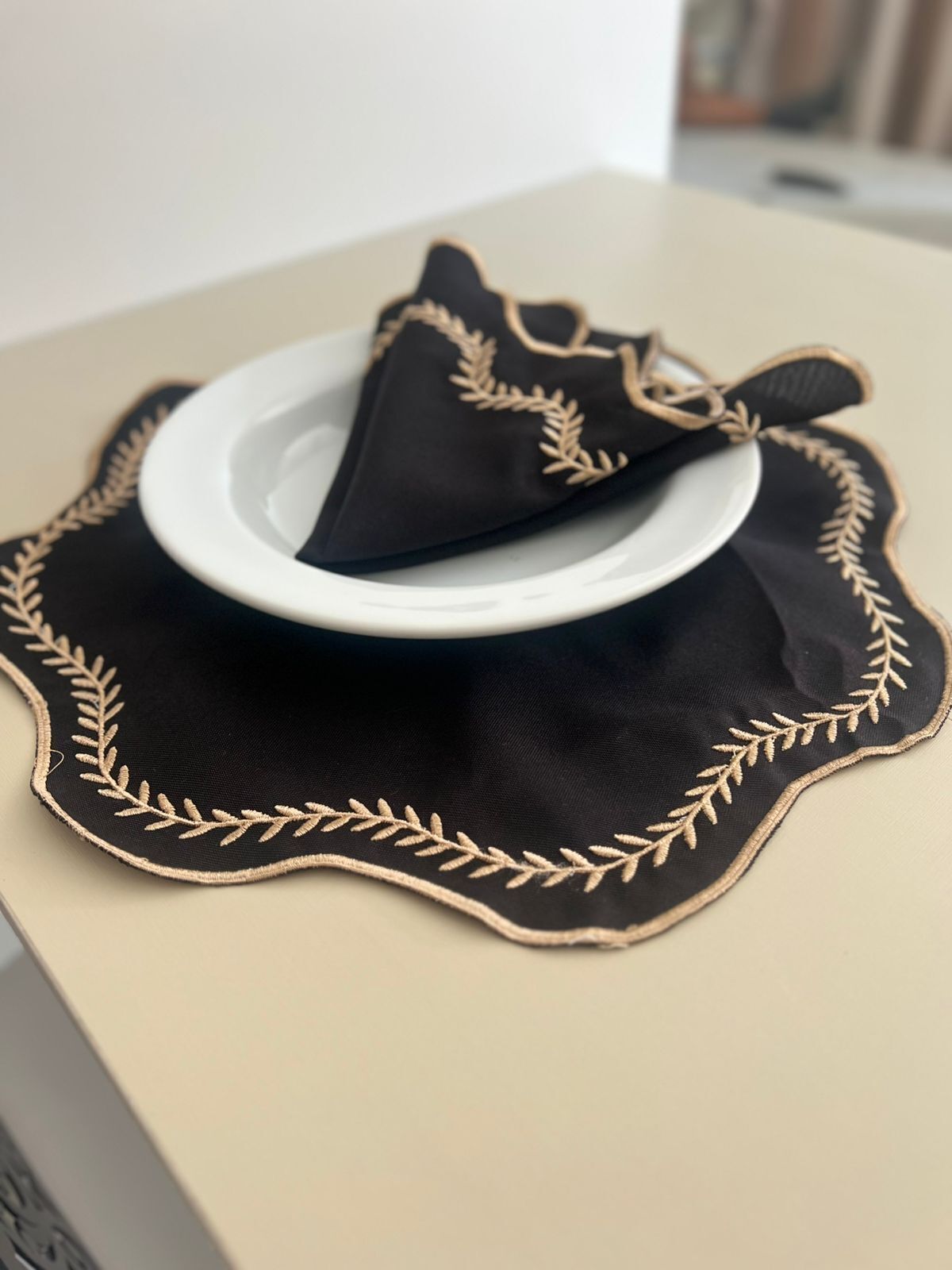 A table with a black tablecloth featuring gold embroidery and a white plate.