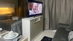 A modern hotel room with a flat-screen TV mounted on a cabinet, a bed with a patterned duvet, a sofa, and a dining area with a table set for two. - Studio 5 minutes from the Metro, Expo Center Norte, Anhembi (Tucuruvi São Paulo)