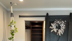 A hallway with a wooden floor, a sliding door with a decorative wreath, and a hanging plant.
