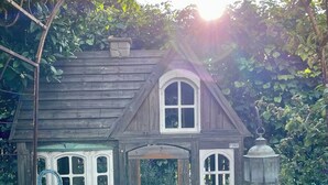A wooden house with a central door, two windows on each side, and a small porch area.