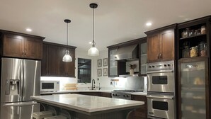 A modern kitchen with stainless steel appliances, a central island with stools, and wooden cabinetry.