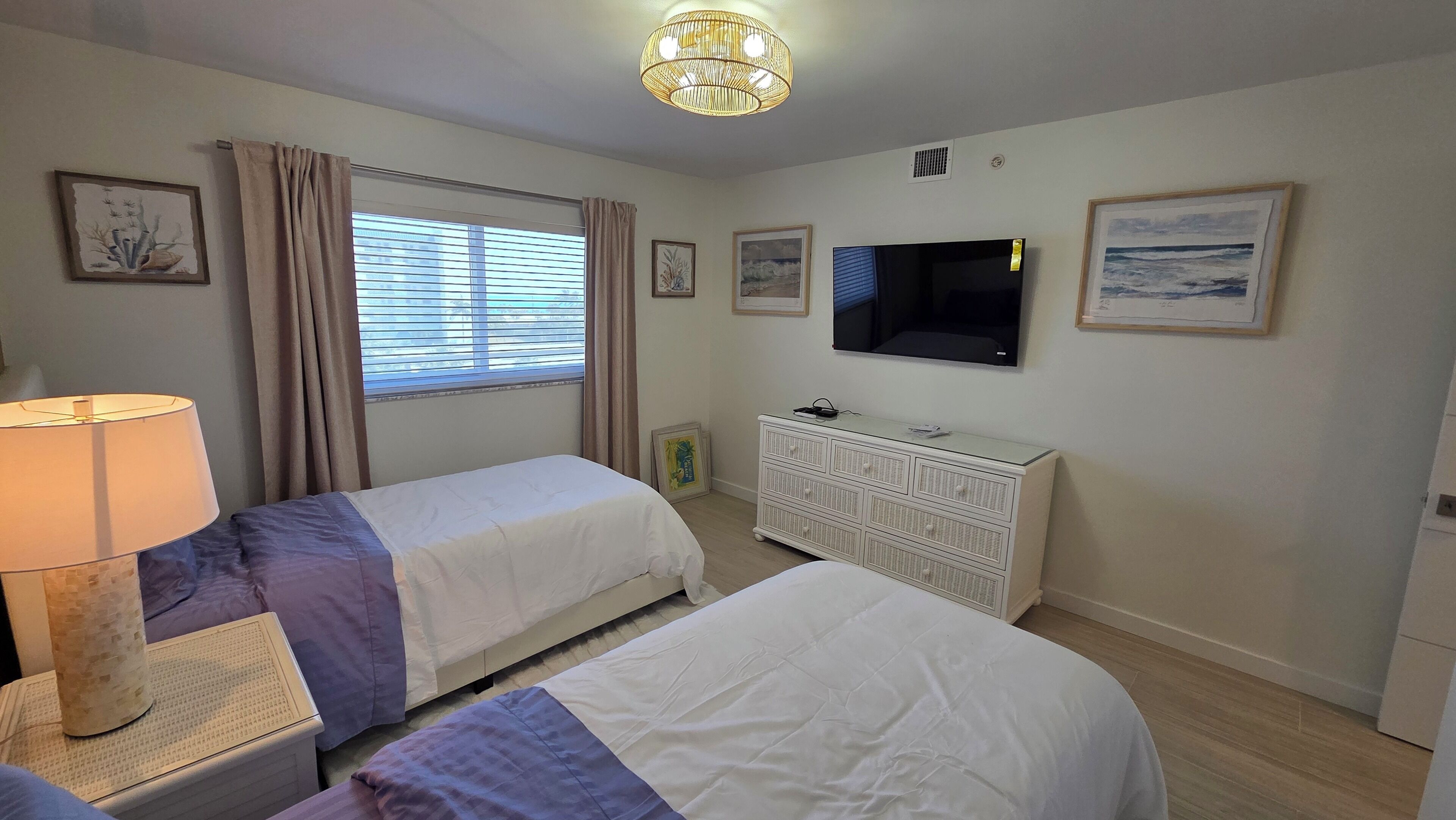 Ein Hotelzimmer mit zwei Betten, einem Fernseher, einer Lampe und einem Fenster mit Vorhängen.