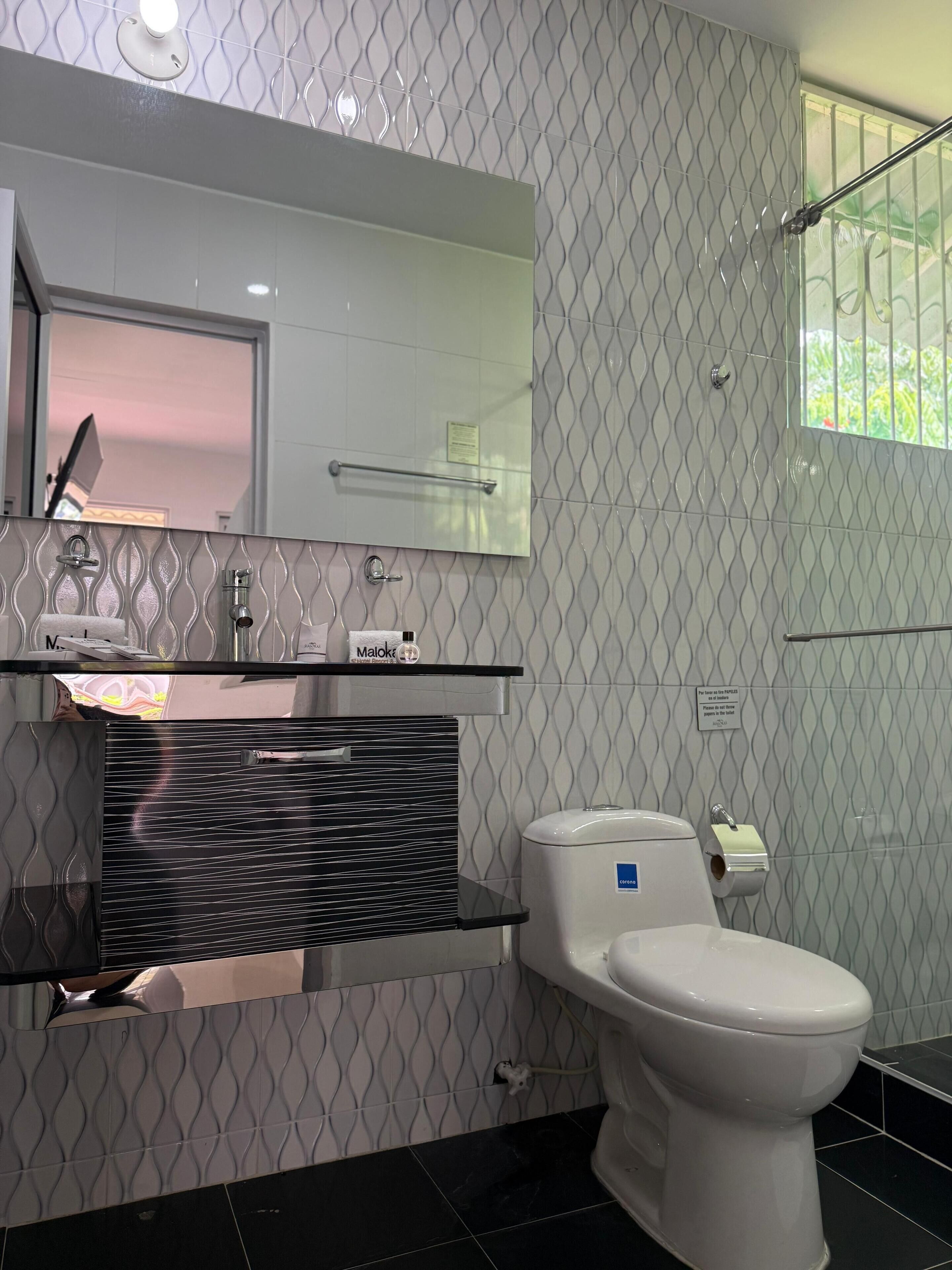 Un baño moderno con pared de azulejos blanco y negro, inodoro blanco, lavabo negro con espejo encima y toallero.