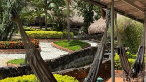 A hammock under a covered area with a view of a landscaped garden, including a water feature and palm trees. - MALOKAS RESORT (Socorro)