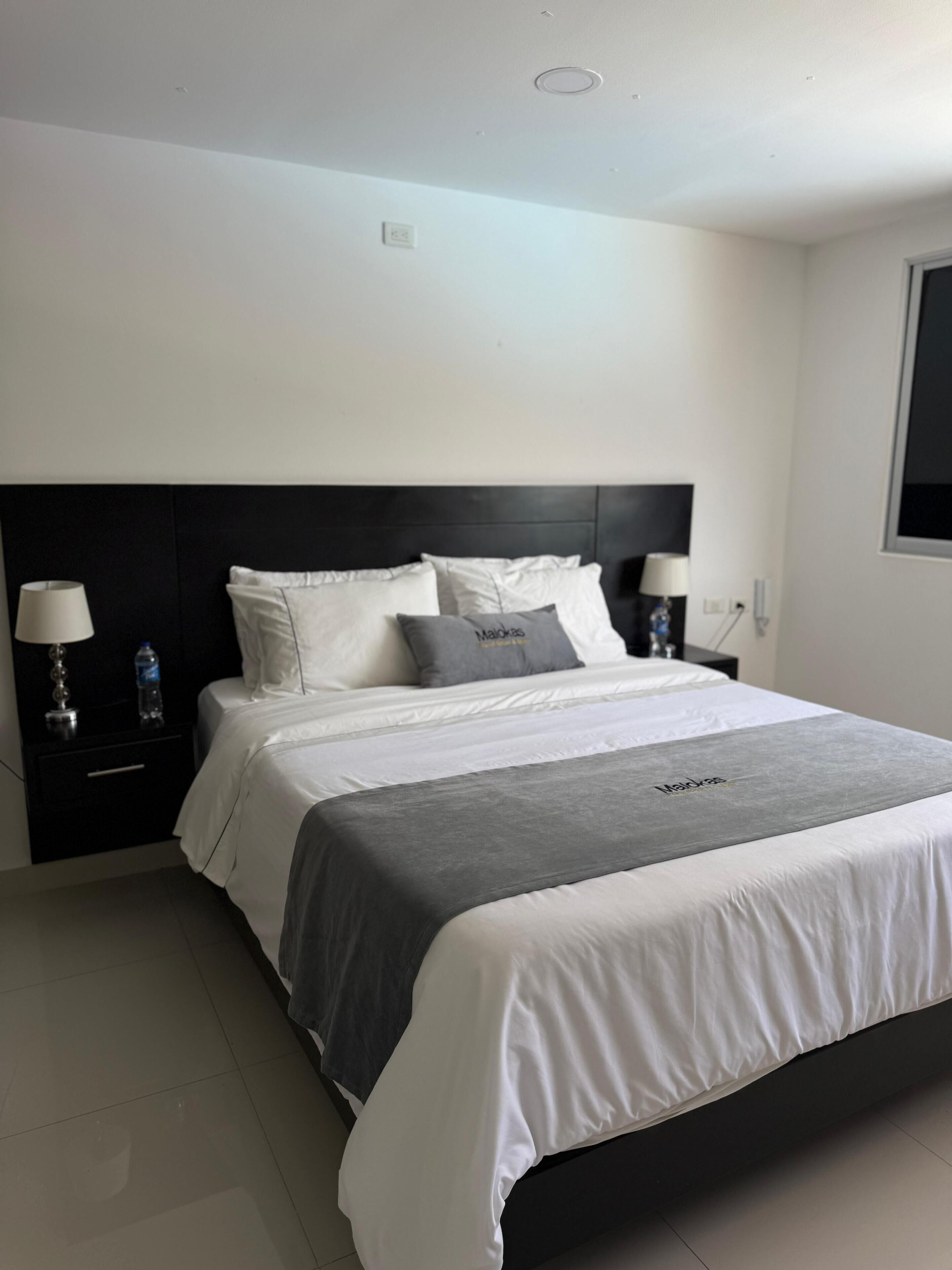 A neatly made bed with white and gray bedding, a dark headboard, and two bedside lamps.