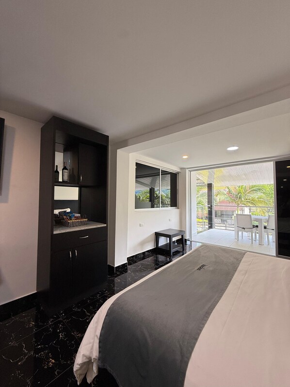 A modern hotel room with a large bed, a dark wooden wardrobe, a small table, and a view of the outdoors through a sliding glass door. - MALOKAS RESORT (Socorro)