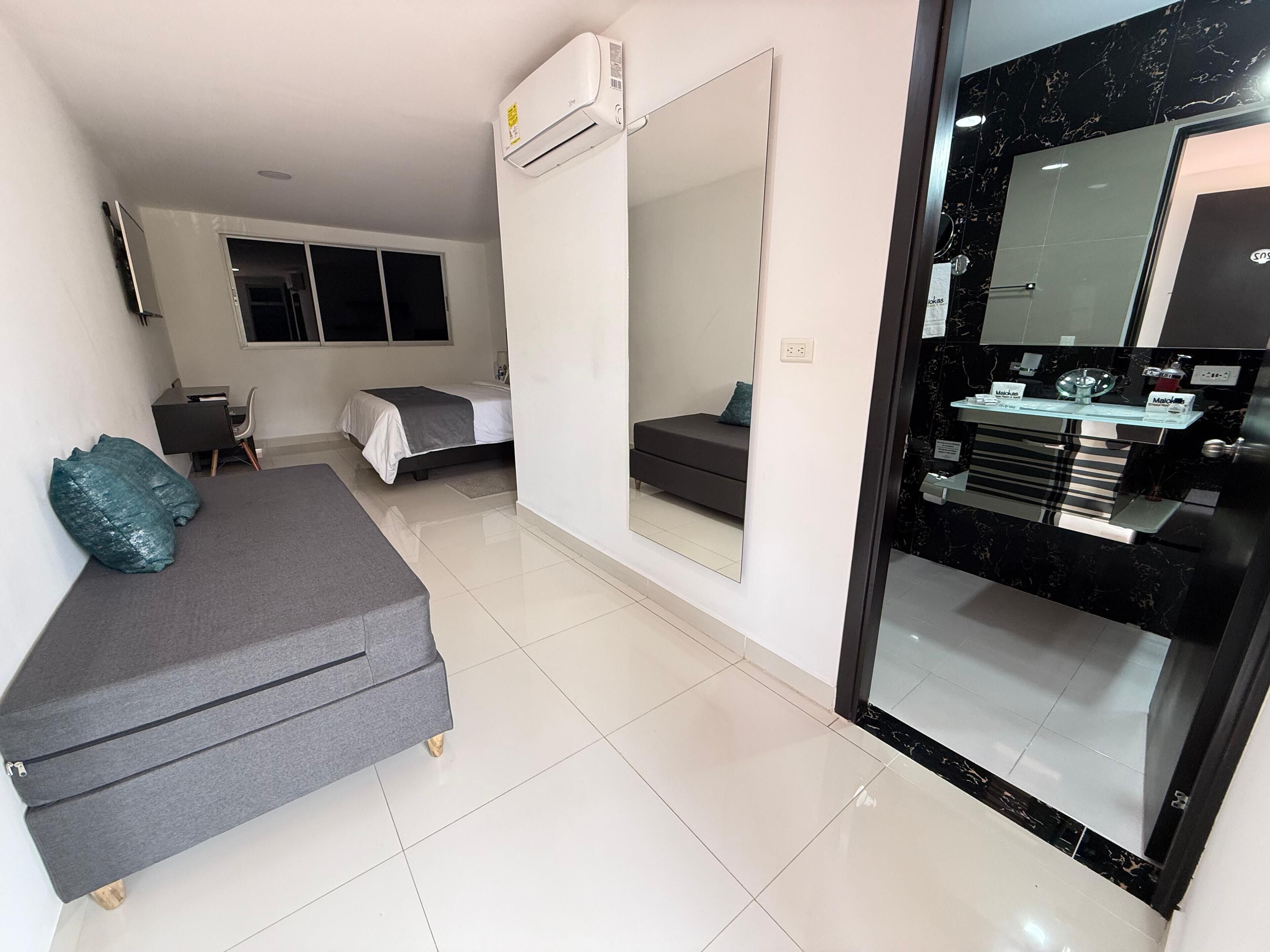 Una habitación de hotel moderna con cama, sofá, escritorio y baño con espejo y lavamanos.