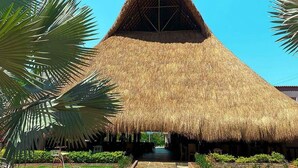 A thatched-roof structure with a central open space, surrounded by greenery and a stone pathway. - MALOKAS RESORT (Socorro)