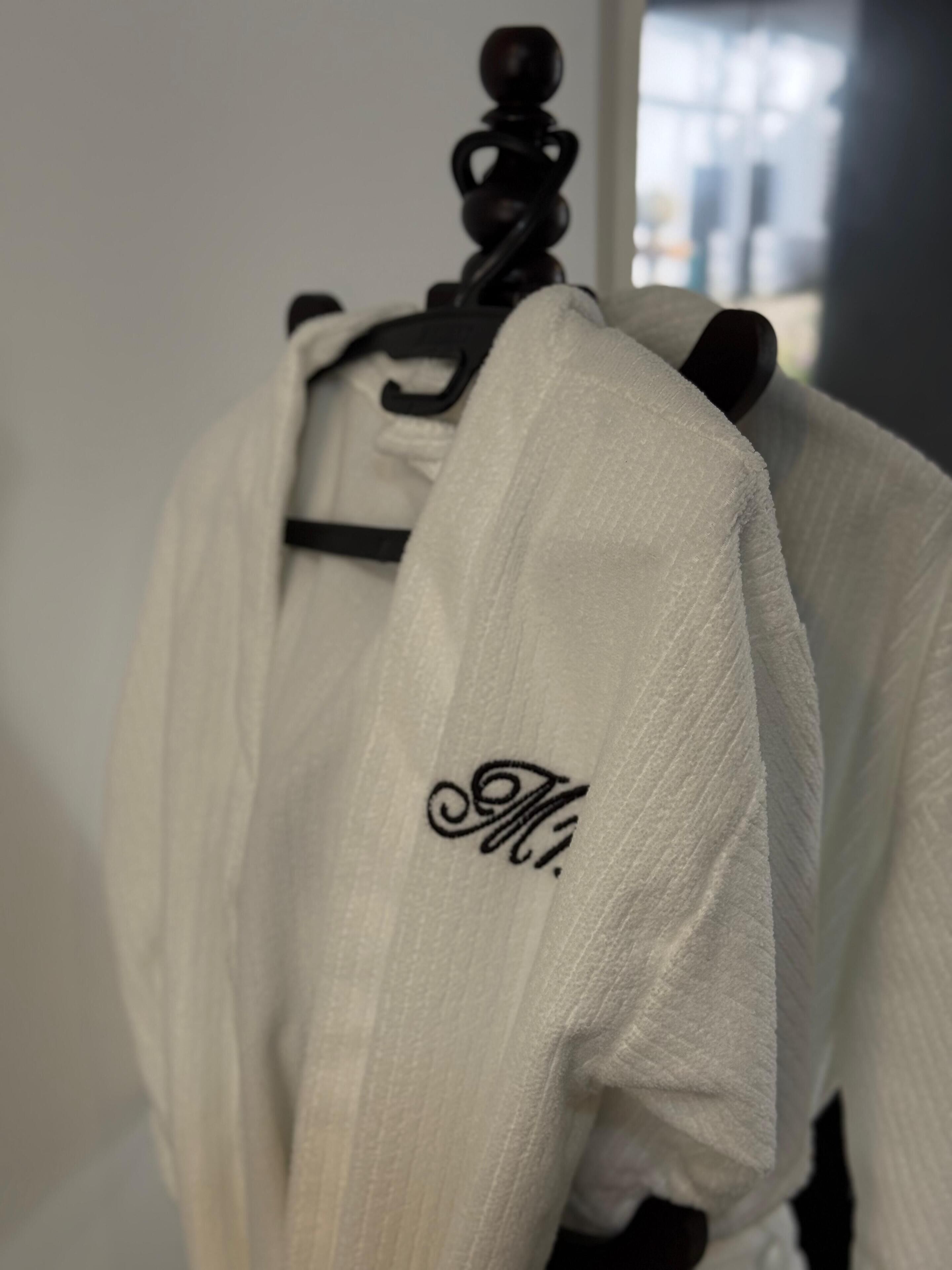 A white robe with a monogram on a black hanger.