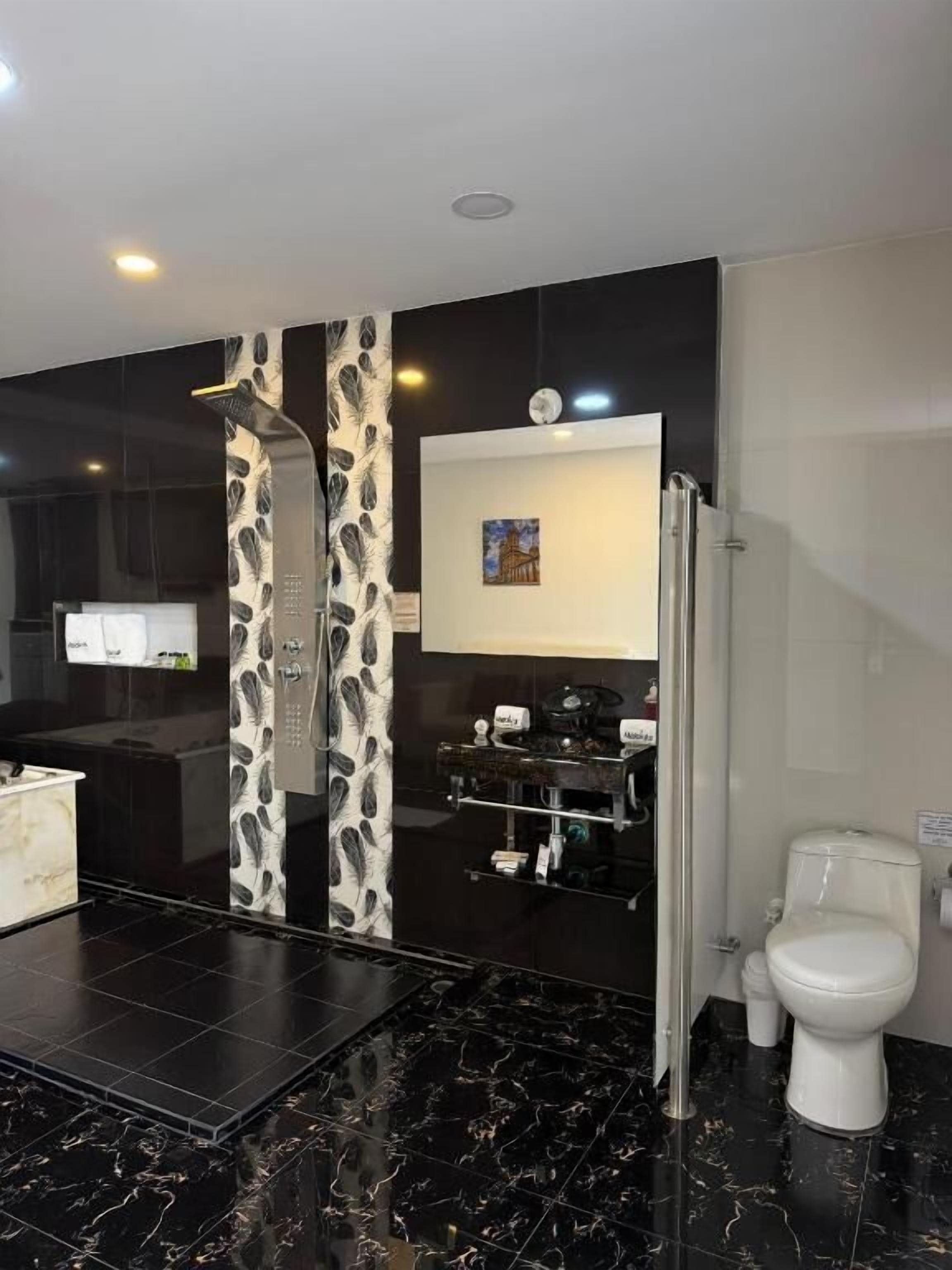 Un baño moderno con piso de mármol blanco y negro, inodoro blanco, ducha y zona de lavamanos.