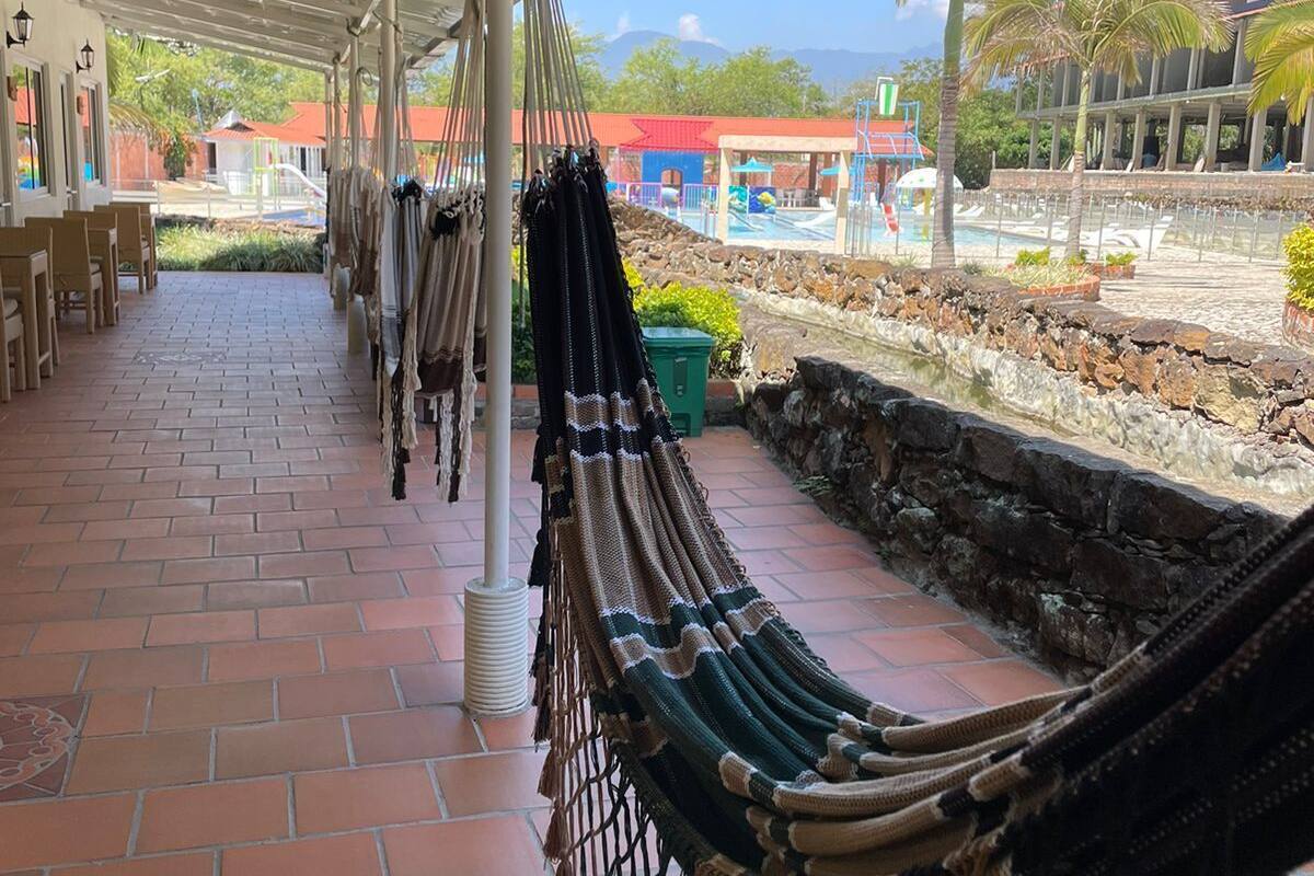 A covered outdoor area with a brick floor, hammocks, and a view of a pool and buildings in the background.