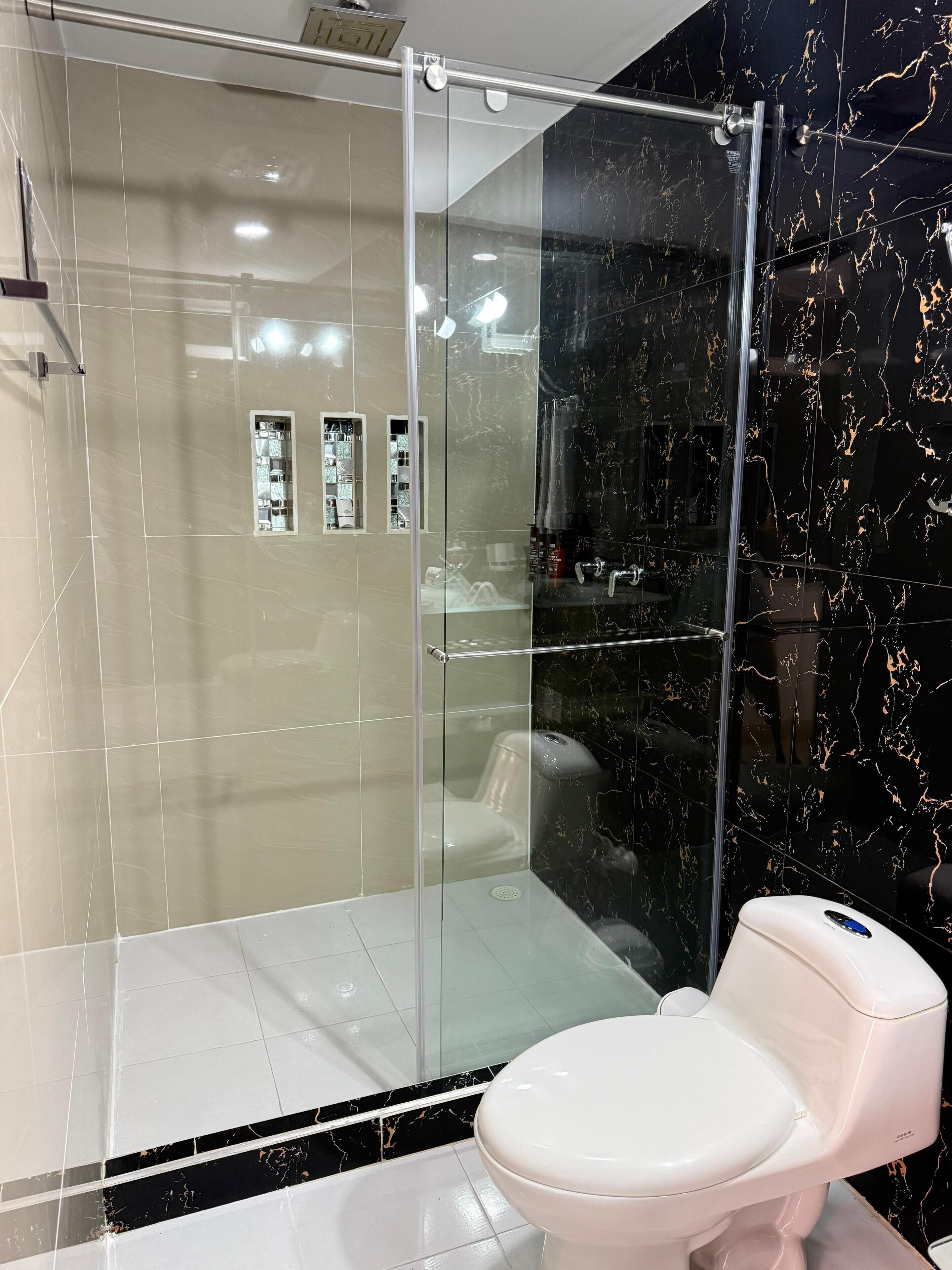 A modern bathroom with a glass-enclosed shower, a white toilet, and a marble-tiled wall.