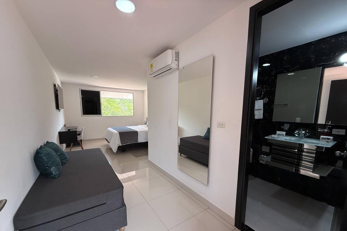 A modern bedroom with a bed, a sofa, a desk, and a large mirror.